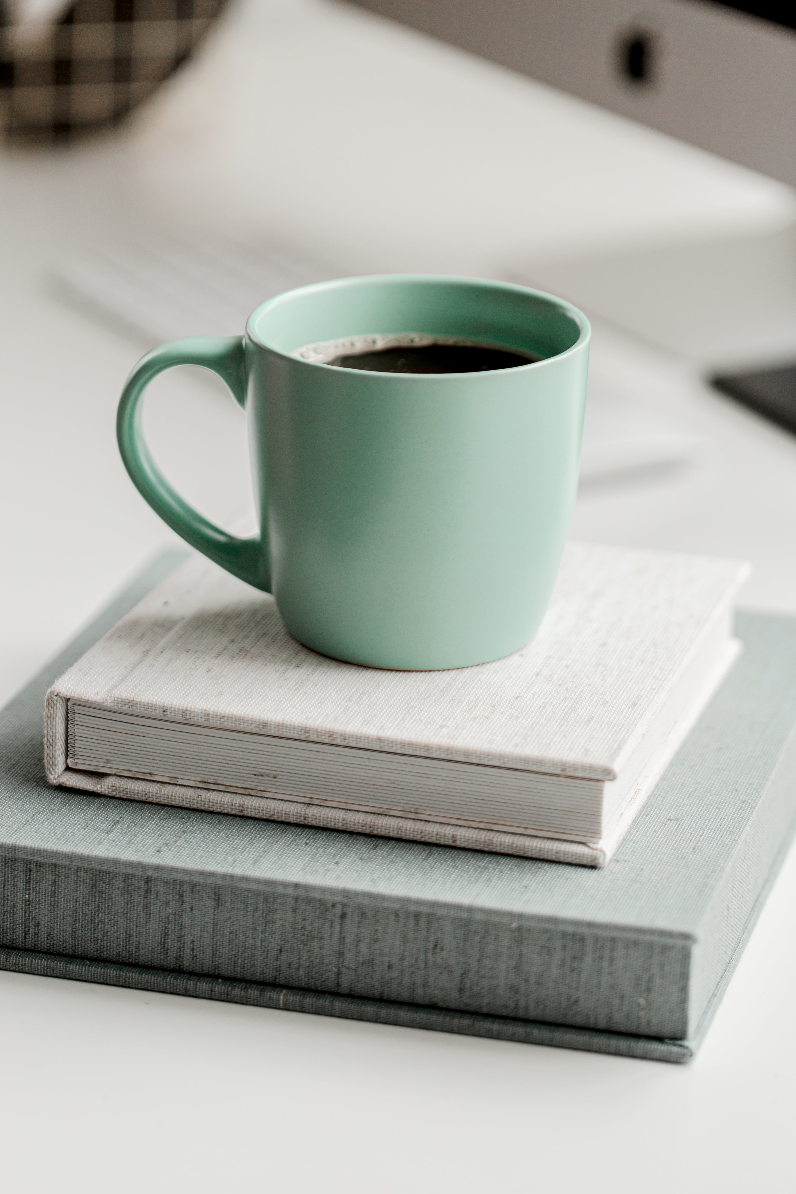 A green mug filled with black coffee sitting on top of two books.